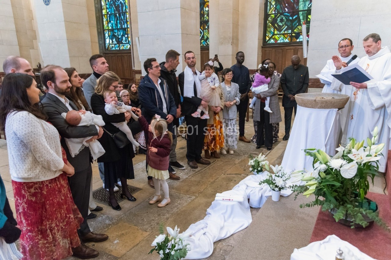 Un groupe de personnes rassemblées dans une église pour une cérémonie de baptême près d'un prêtre et d'une cuve baptismale.