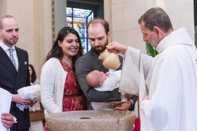Un couple s'embrasse dans une rue pavée devant un bâtiment rose couvert de végétation.