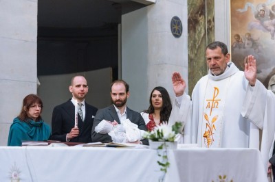 Un couple s'embrasse dans une rue pavée devant un bâtiment rose couvert de végétation.