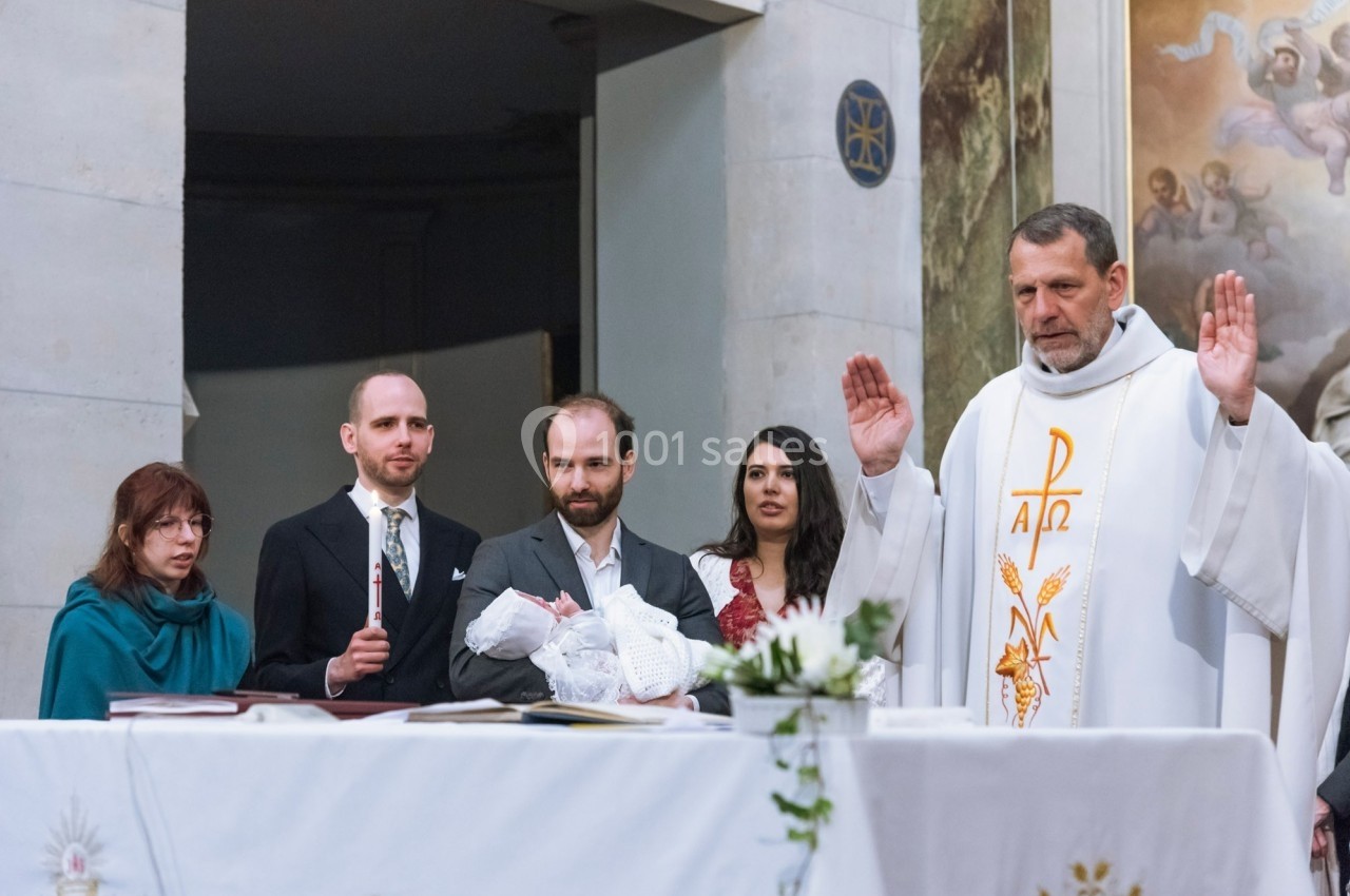 Un prêtre bénit un enfant lors d'une cérémonie religieuse, entouré de quatre adultes devant un autel.