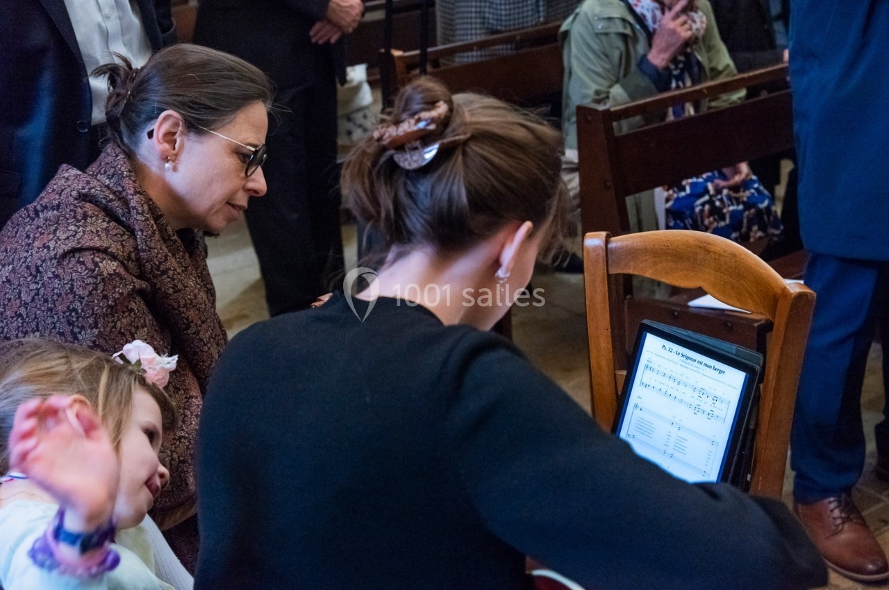 Une femme joue de la guitare en lisant une partition sur une tablette, entourée de personnes assises.