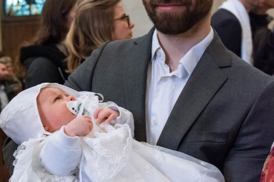 Un couple s'embrasse dans une rue pavée devant un bâtiment rose couvert de végétation.
