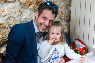 Un couple s'embrasse dans une rue pavée devant un bâtiment rose couvert de végétation.