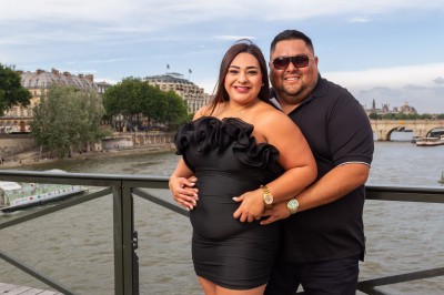 Un couple s'embrasse dans une rue pavée devant un bâtiment rose couvert de végétation.