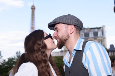 Un couple s'embrasse dans une rue pavée devant un bâtiment rose couvert de végétation.