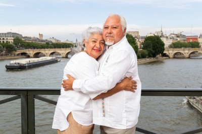 Un couple s'embrasse dans une rue pavée devant un bâtiment rose couvert de végétation.