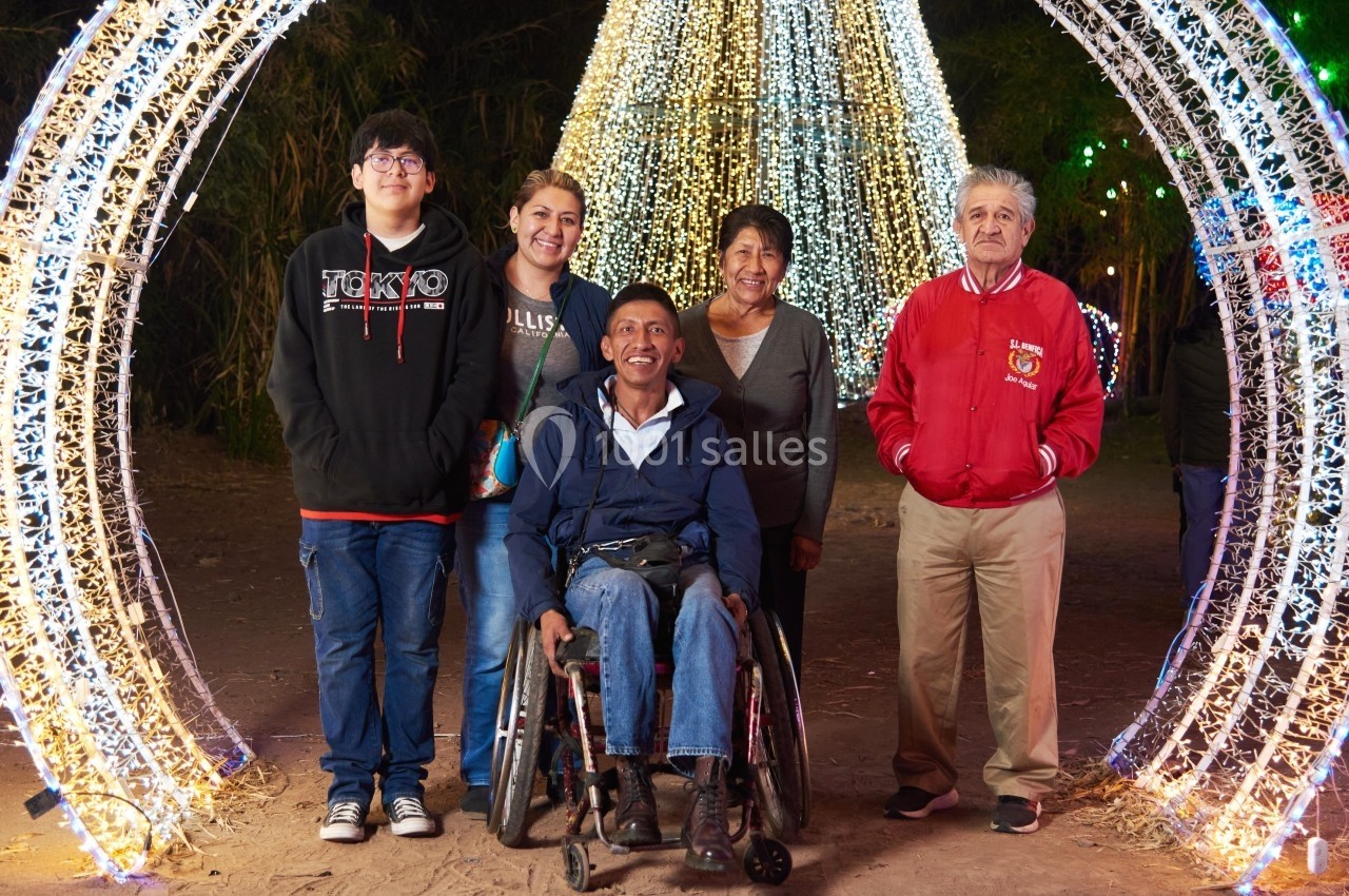 Un groupe de cinq personnes, dont une en fauteuil roulant, pose devant des décorations lumineuses en extérieur.
