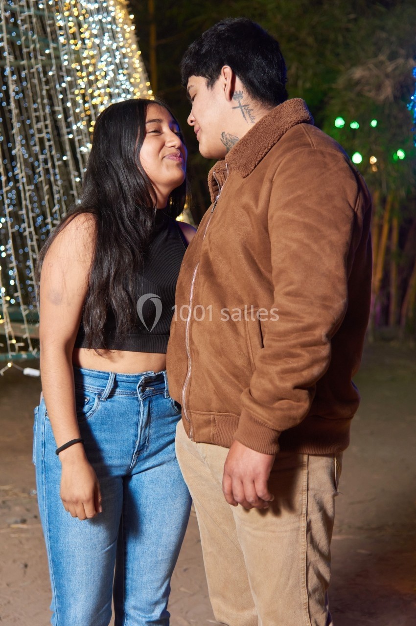 Un couple se regarde avec complicité devant des décorations lumineuses dans un environnement extérieur.
