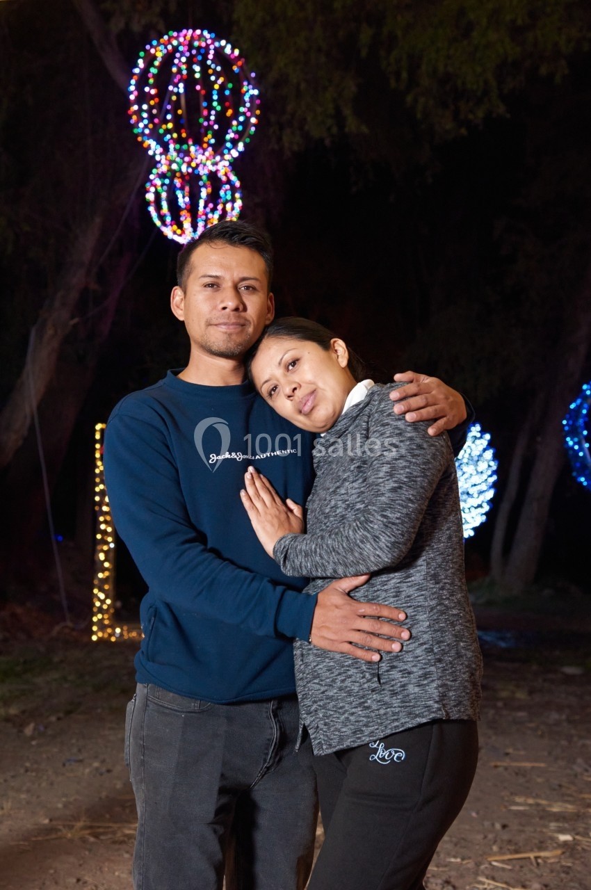 Un couple pose enlacé devant des décorations lumineuses colorées dans un environnement extérieur nocturne.