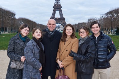 Un groupe de personnes pose devant la tour Eiffel par temps nuageux, dans un espace dégagé bordé d'arbres.
