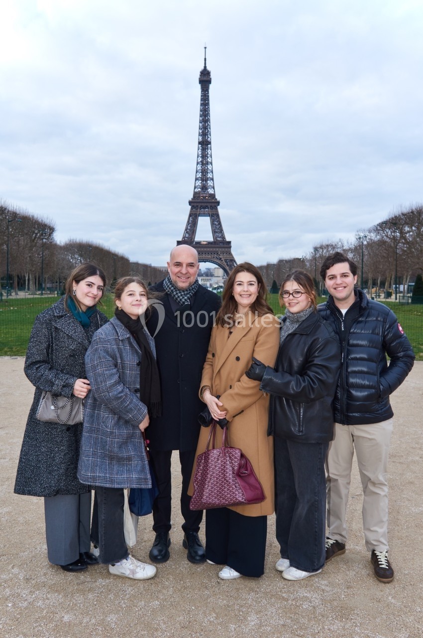 Un groupe de six personnes pose devant la tour Eiffel par temps nuageux.