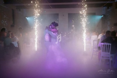 Un couple danse au centre d'une piste éclairée par des projecteurs violets et des étincelles, entouré de spectateurs.