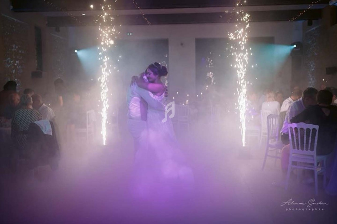 Un couple danse au milieu d'une salle éclairée par des étincelles et une ambiance de fumée légère.