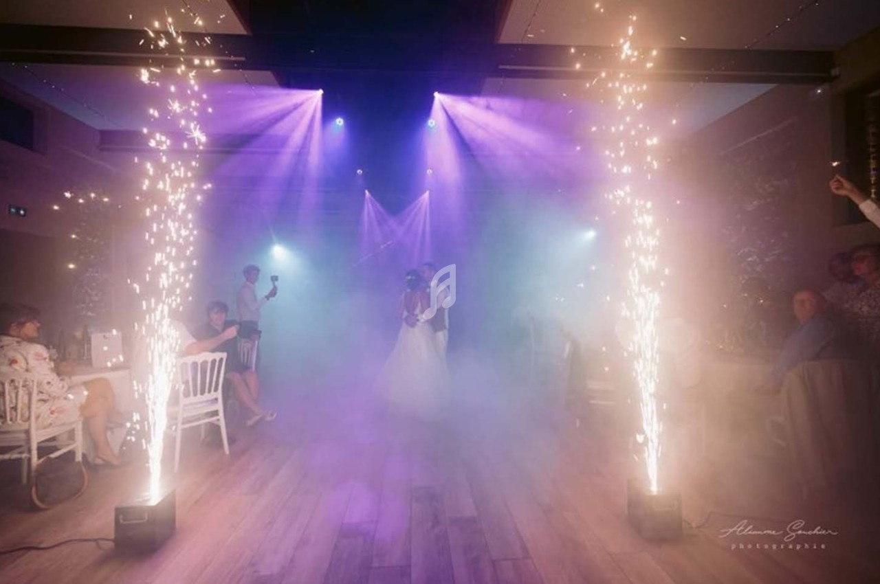 Un couple danse au centre d'une salle éclairée par des projecteurs colorés et des gerbes d'étincelles.