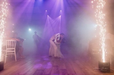 Un couple danse au centre d'une piste éclairée par des projecteurs violets et des étincelles, entouré de spectateurs.