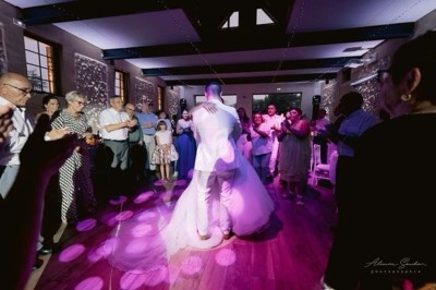 Un couple danse au centre d'une salle éclairée, entouré d'invités applaudissant sur une piste en bois.