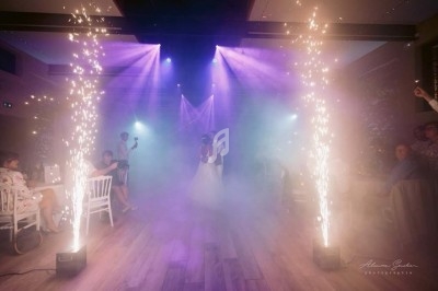Un couple danse au centre d'une salle éclairée par des projecteurs violets, entouré de jets d'étincelles et de fumée.
