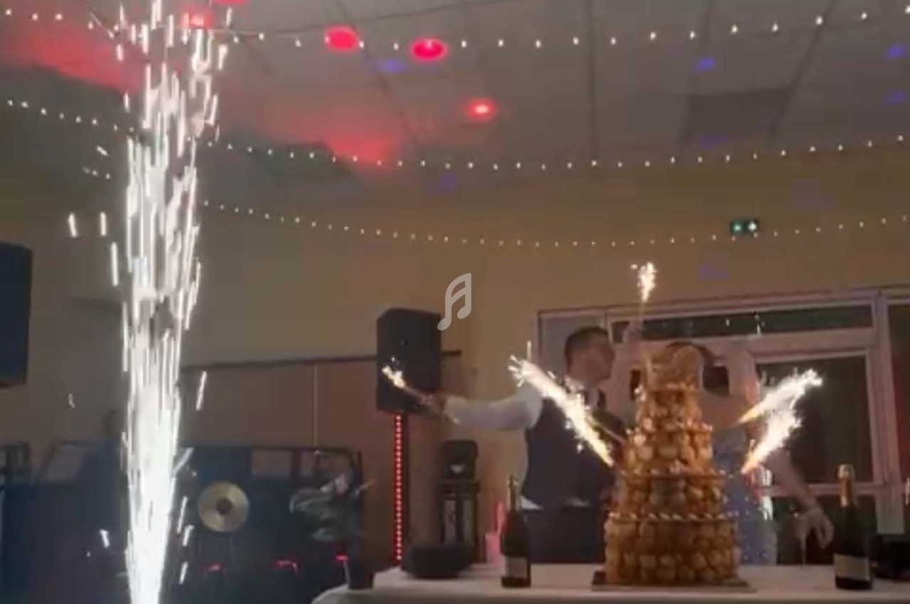 Un couple célèbre devant une pièce montée éclairée par des fontaines lumineuses dans une salle décorée.