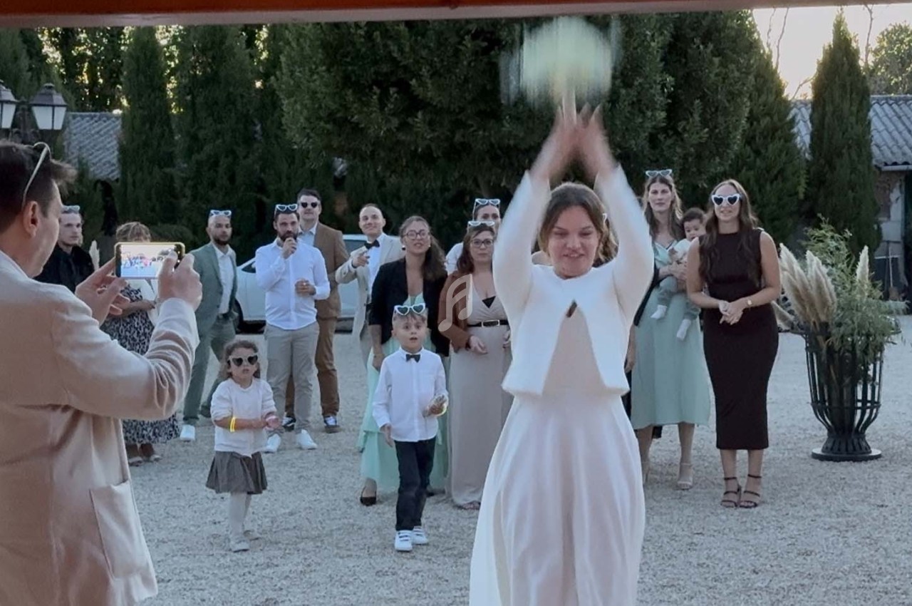 Une mariée lance son bouquet vers un groupe d'invités rassemblés dans une cour extérieure.
