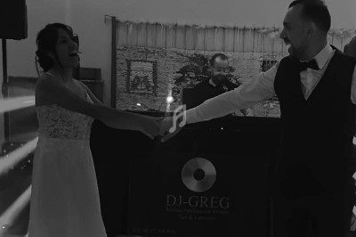 Un couple en tenue de mariage danse devant un DJ dans une salle éclairée par des jeux de lumière.