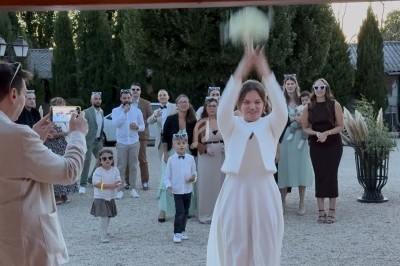 Une mariée lance son bouquet de fleurs vers un groupe d'invités lors d'une réception en extérieur.