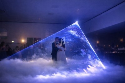 Un couple danse au centre d'une projection lumineuse en forme de pyramide, entouré d'un sol couvert de fumée.