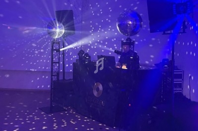 Deux DJ mixent derrière une table éclairée, entourés de lumières et de boules à facettes dans une ambiance festive.