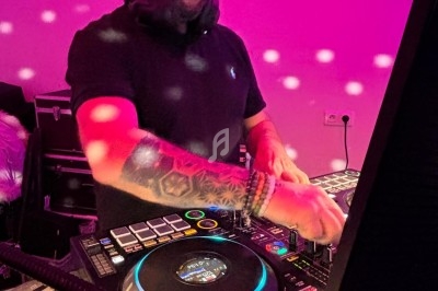 Un DJ mixant de la musique sur une table de mixage dans une ambiance lumineuse rose et festive.
