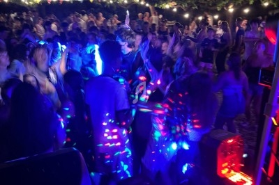 Foule dansante en soirée en plein air, éclairée par des lumières colorées et entourée de guirlandes lumineuses.