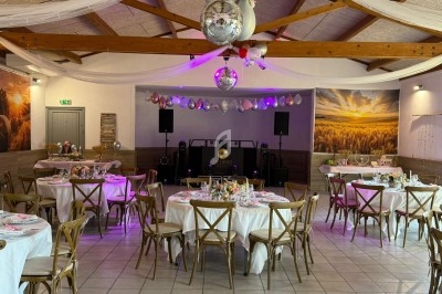 Salle décorée pour un événement avec tables rondes dressées, guirlandes, ballons et piste de danse équipée.