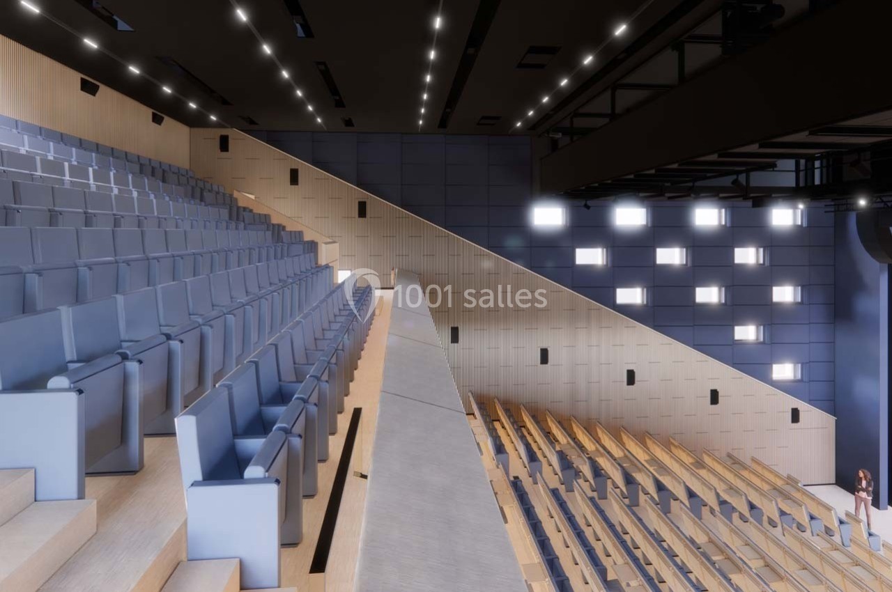 Salle de spectacle moderne avec gradins en bois et sièges bleus, éclairée par des spots et des panneaux lumineux.