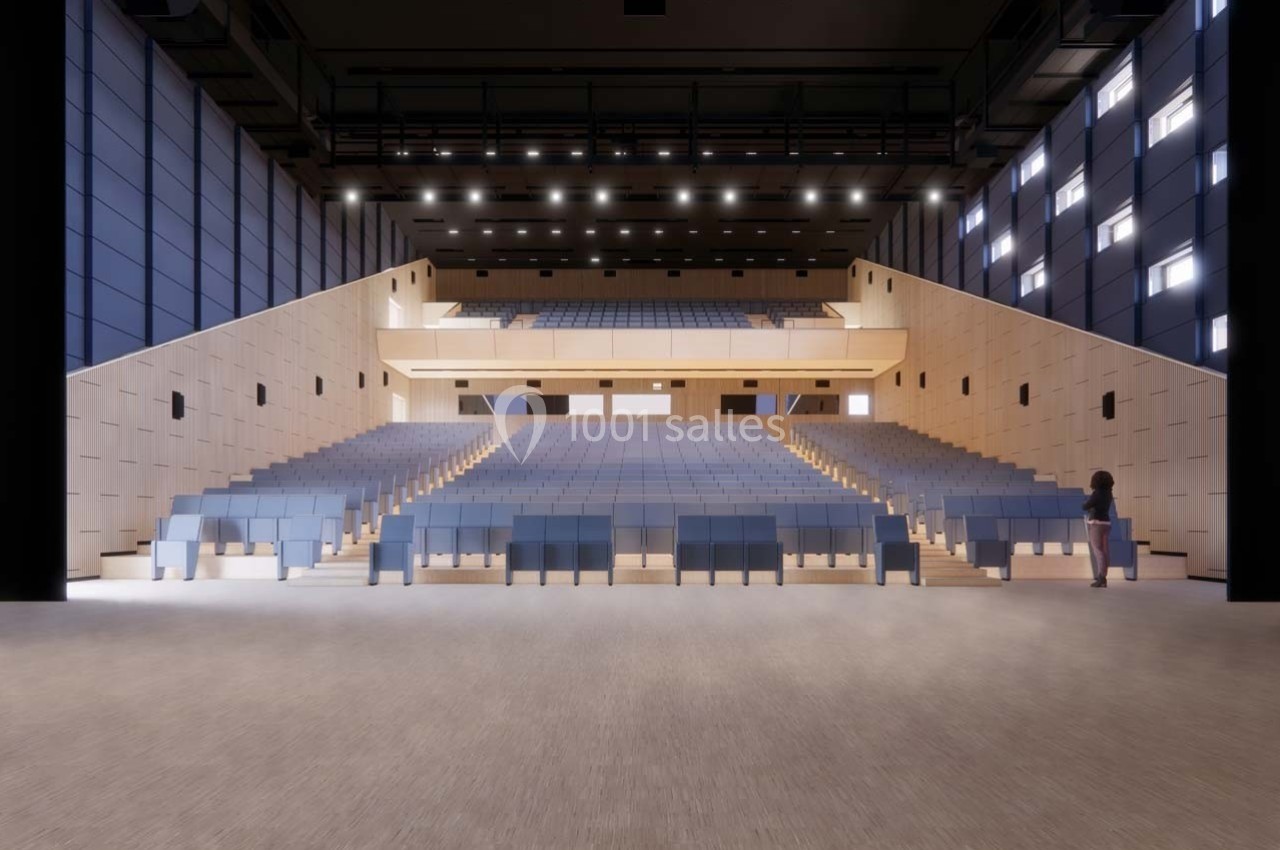 Vue intérieure d'un auditorium vide avec des rangées de sièges bleus, éclairage artificiel et une personne debout à droite.