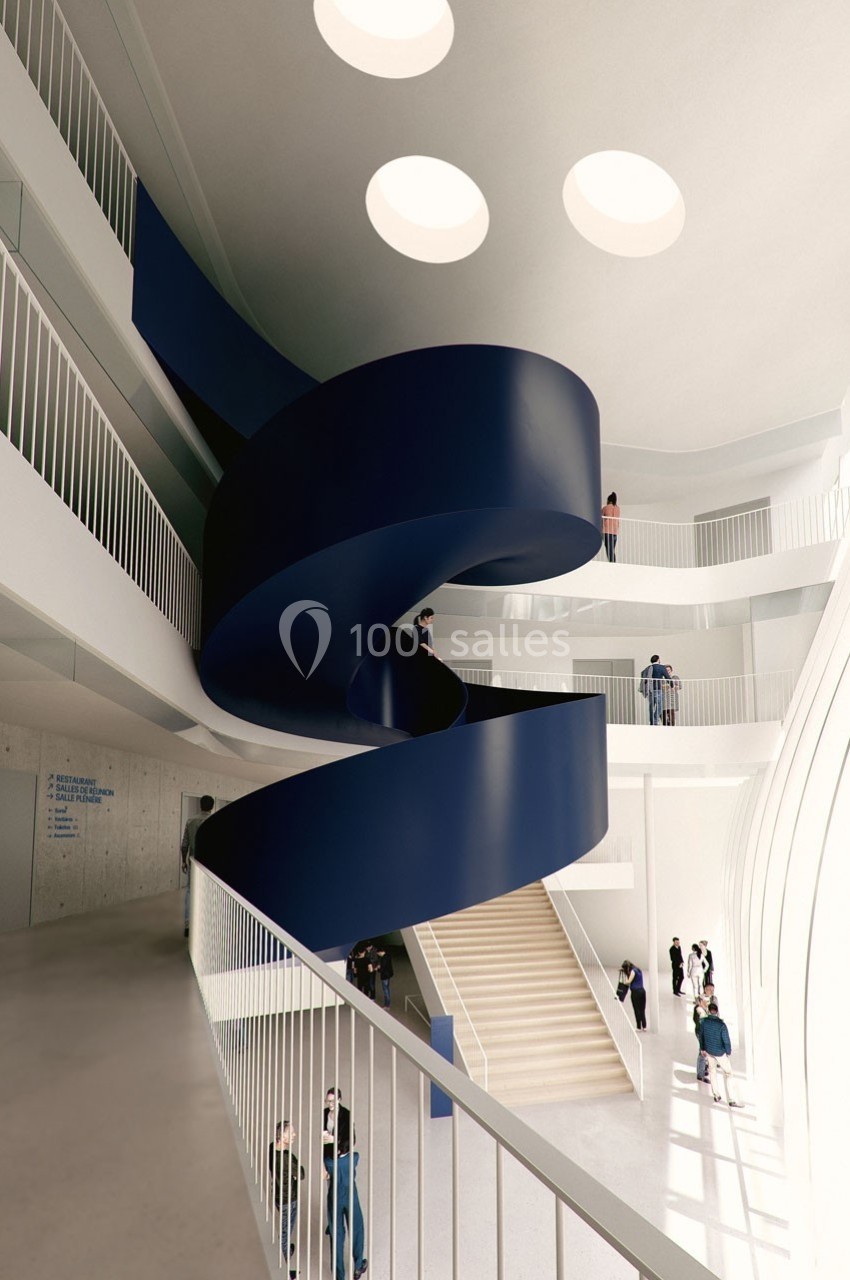 Escalier hélicoïdal bleu au centre d'un bâtiment moderne avec balustrades blanches et puits de lumière circulaires.