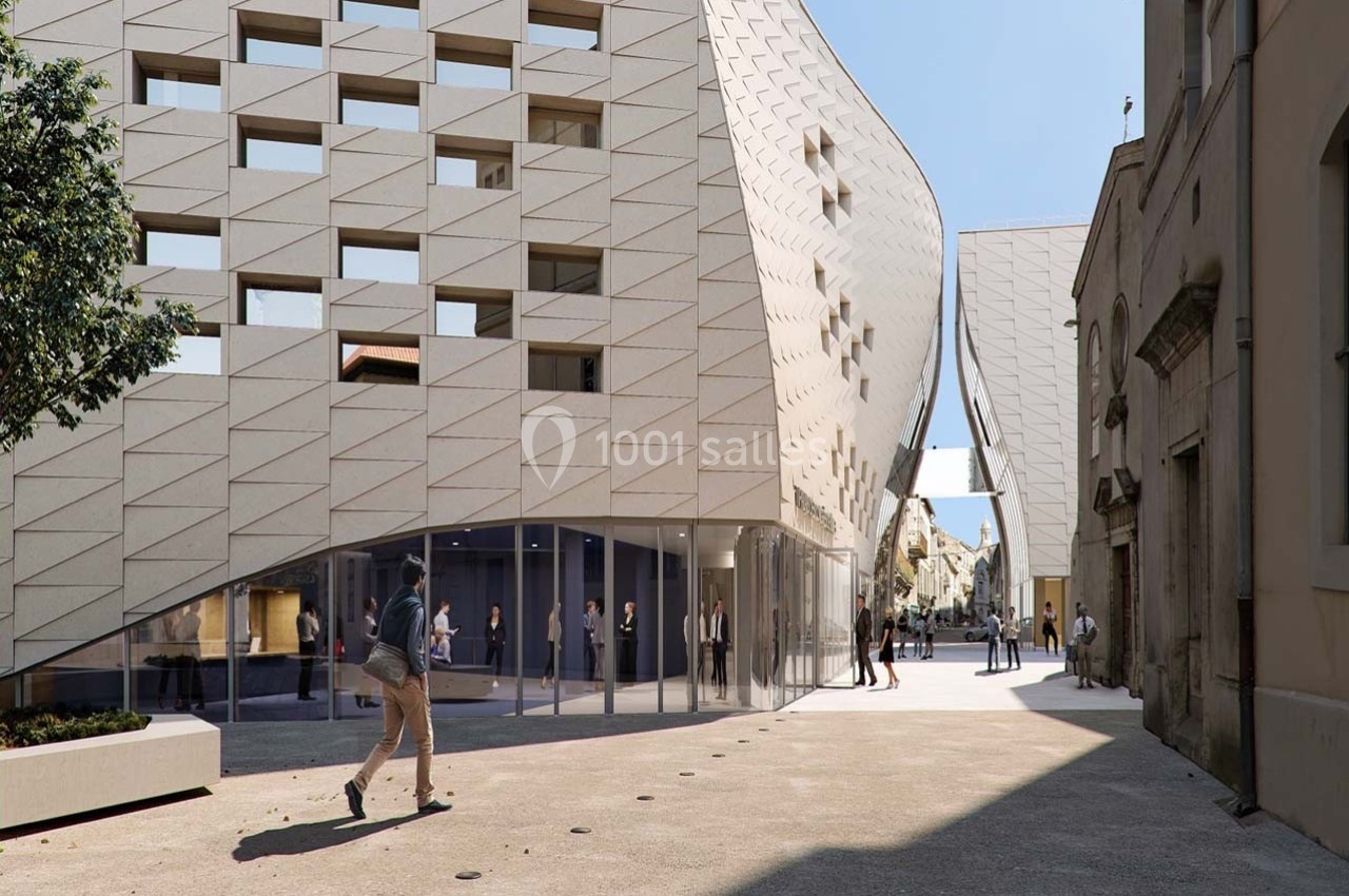 Façade moderne d'un bâtiment avec des motifs géométriques, donnant sur une place piétonne ensoleillée.