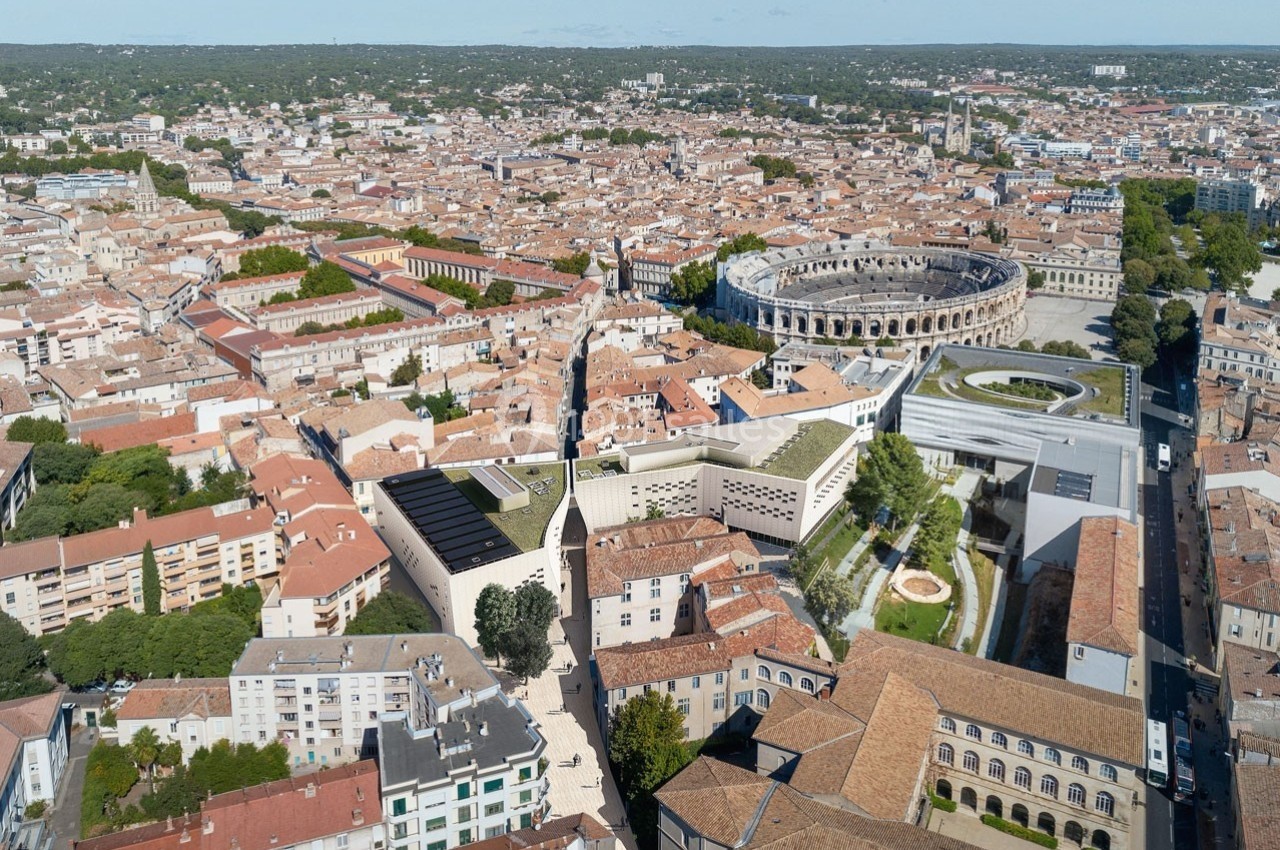 Vue aérienne de la ville de Nîmes, montrant les toits, les arènes romaines et des bâtiments modernes environnants.