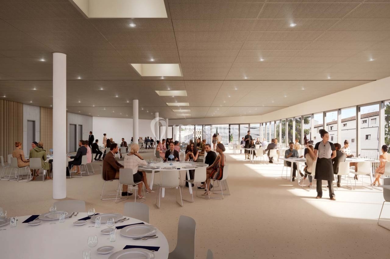 Salle lumineuse avec de grandes baies vitrées, occupée par des convives assis à des tables rondes et des serveurs en service.