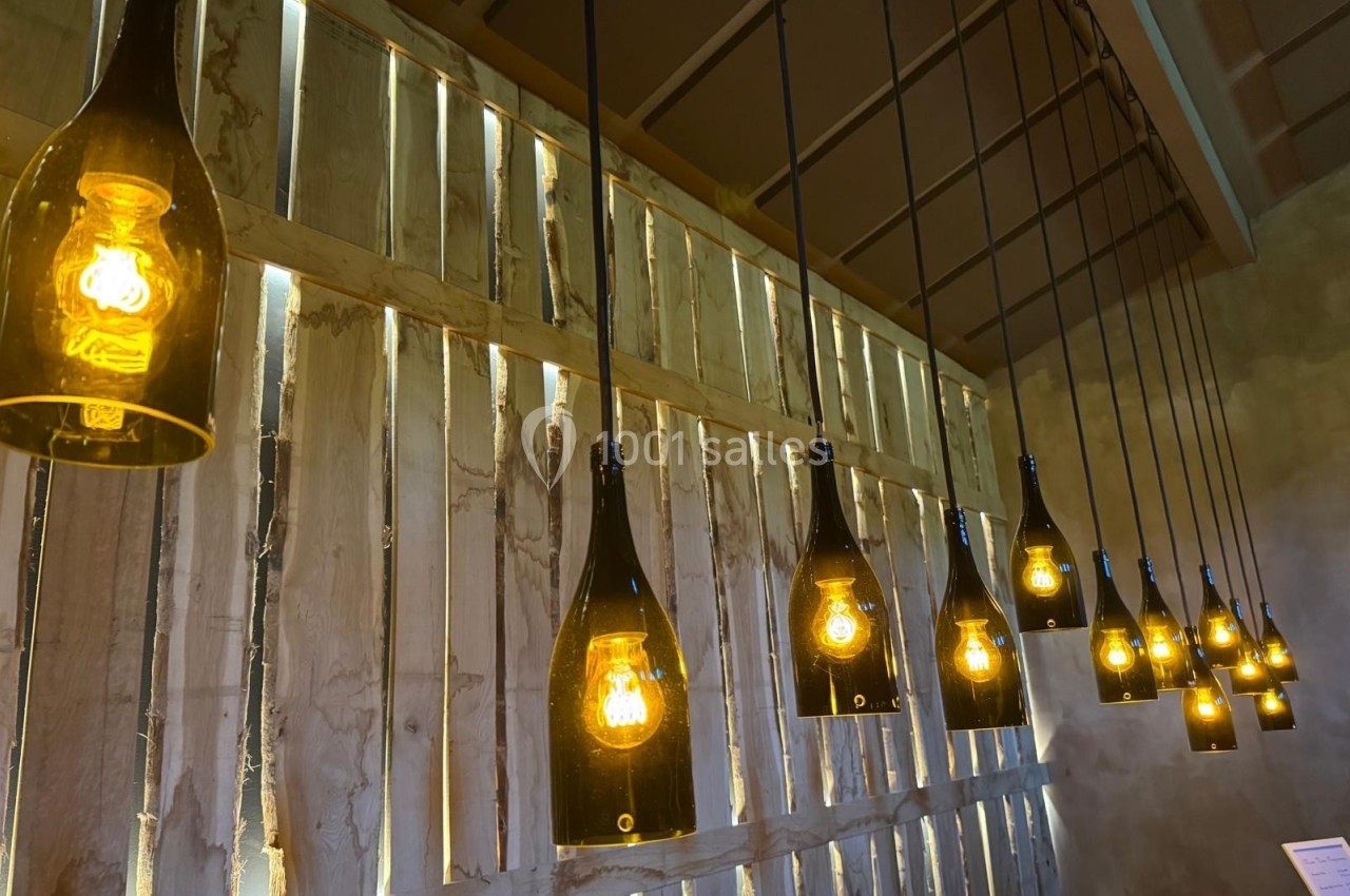 Suspensions lumineuses fabriquées à partir de bouteilles en verre recyclées, alignées devant un mur en bois brut.