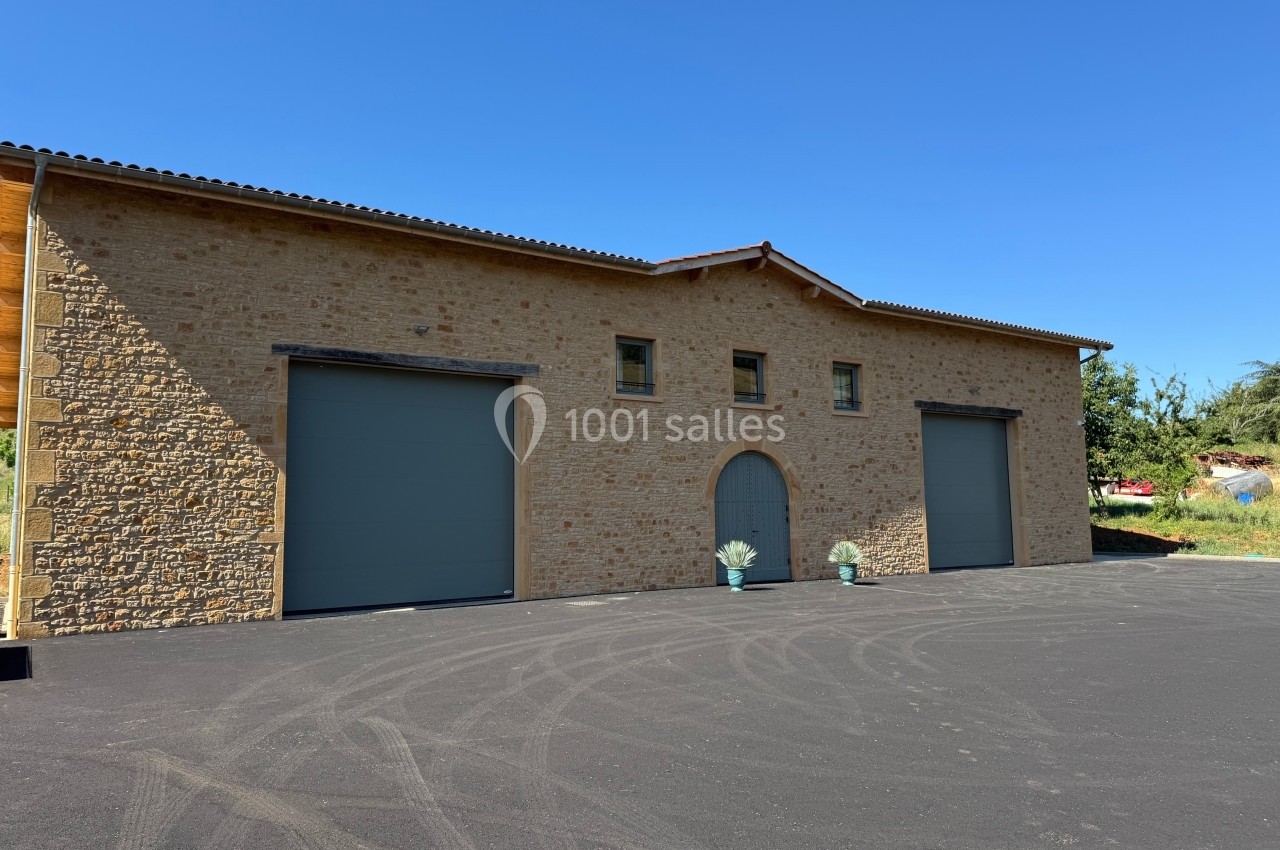 Façade d'un bâtiment en pierre avec trois portes de garage grises et un sol en asphalte noir.
