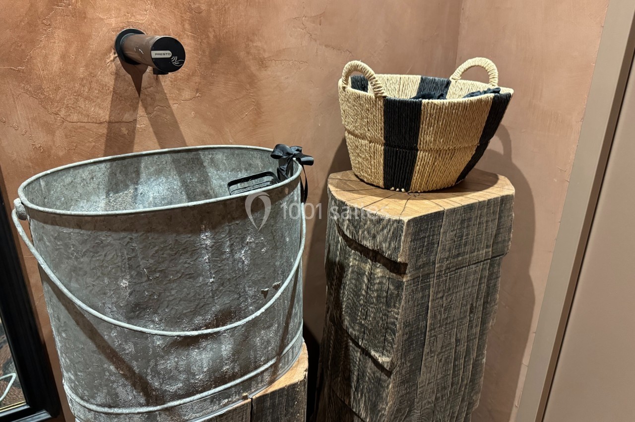 Un seau en métal et un panier en osier posé sur des blocs de bois brut contre un mur texturé brun.