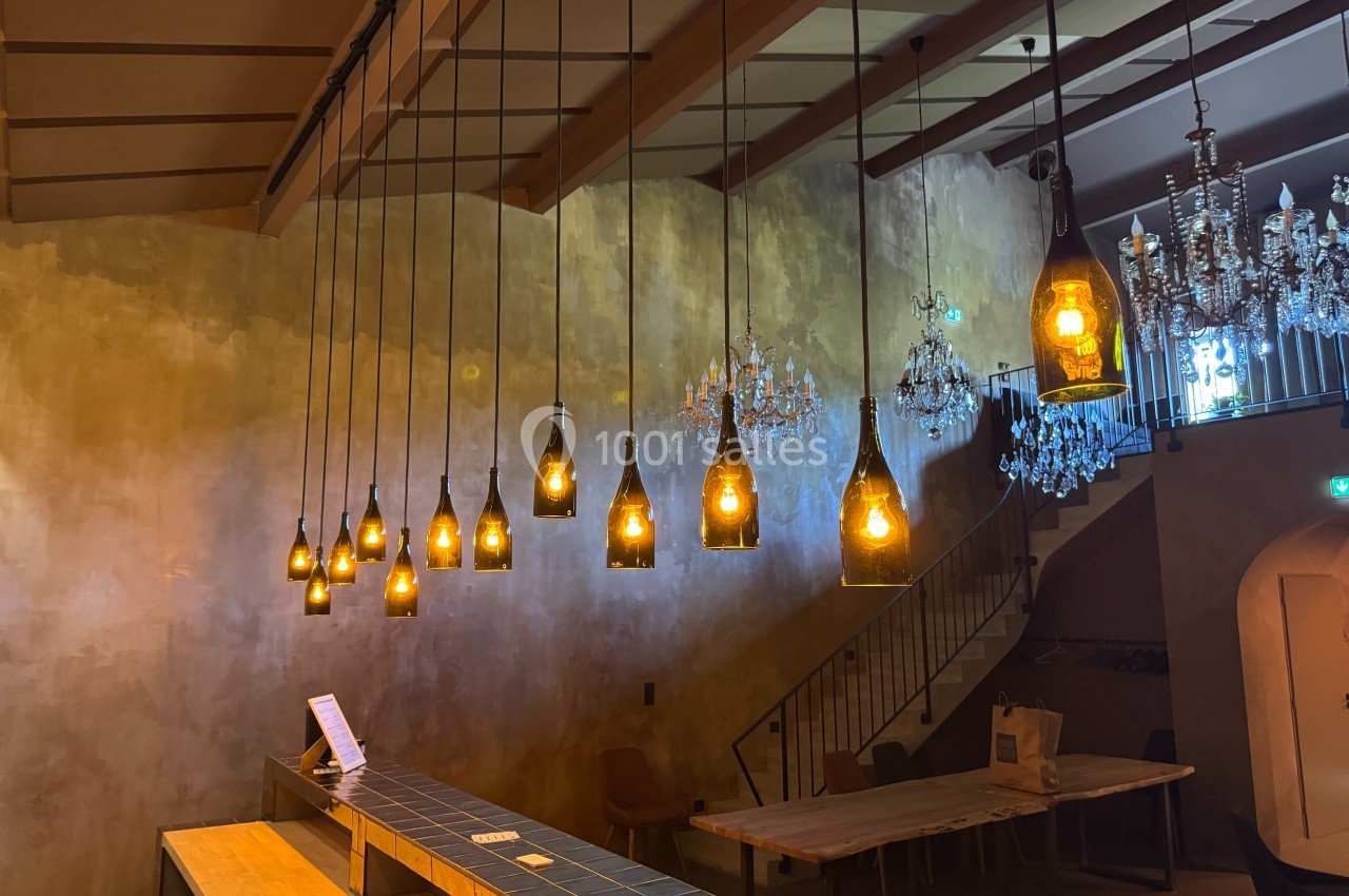 Suspensions lumineuses en bouteilles recyclées éclairant un espace intérieur avec murs texturés et tables en bois.