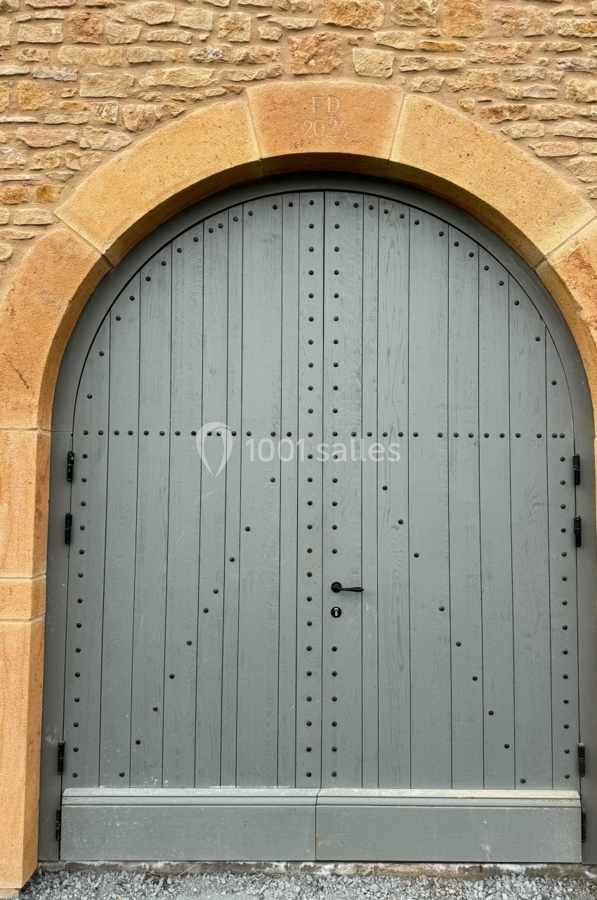 Porte en bois grise à double battant, encadrée par une arche en pierre sur un mur de briques.