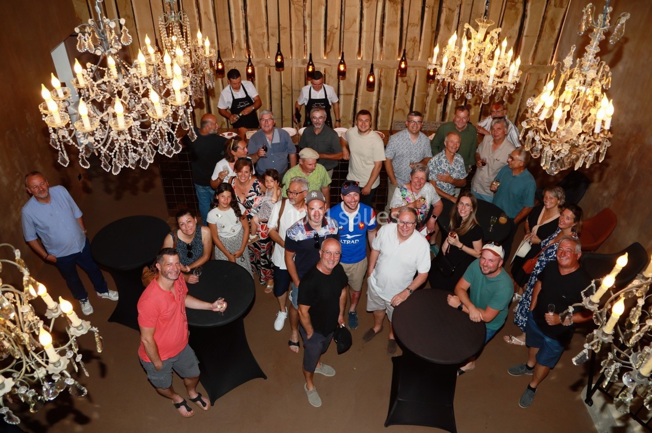 Groupe de personnes rassemblées dans une salle décorée de lustres, autour de tables hautes.