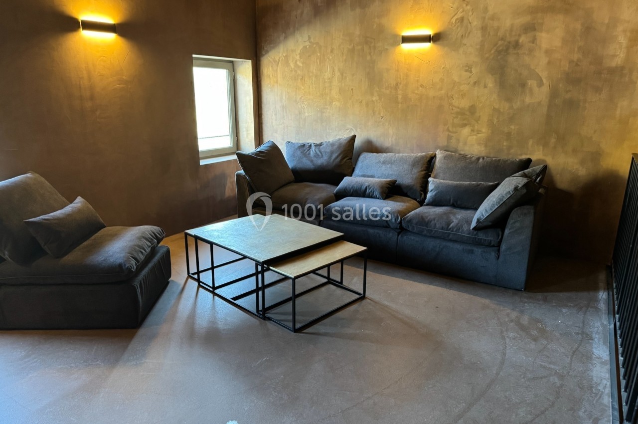 Salon avec canapé gris, fauteuil assorti, table basse en métal et bois, murs texturés et éclairage mural doux.