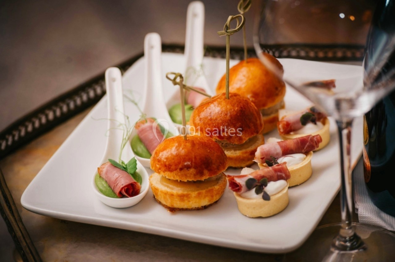 Assortiment de bouchées apéritives sur un plateau, comprenant mini-burgers, cuillères garnies et tartelettes.