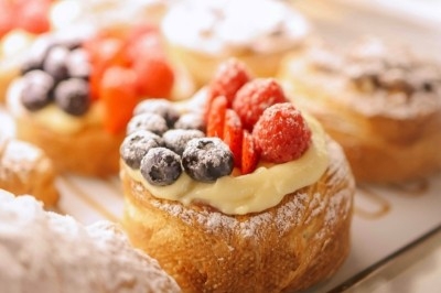 Pâtisseries garnies de crème, framboises et myrtilles, disposées sur un présentoir en vitrine.