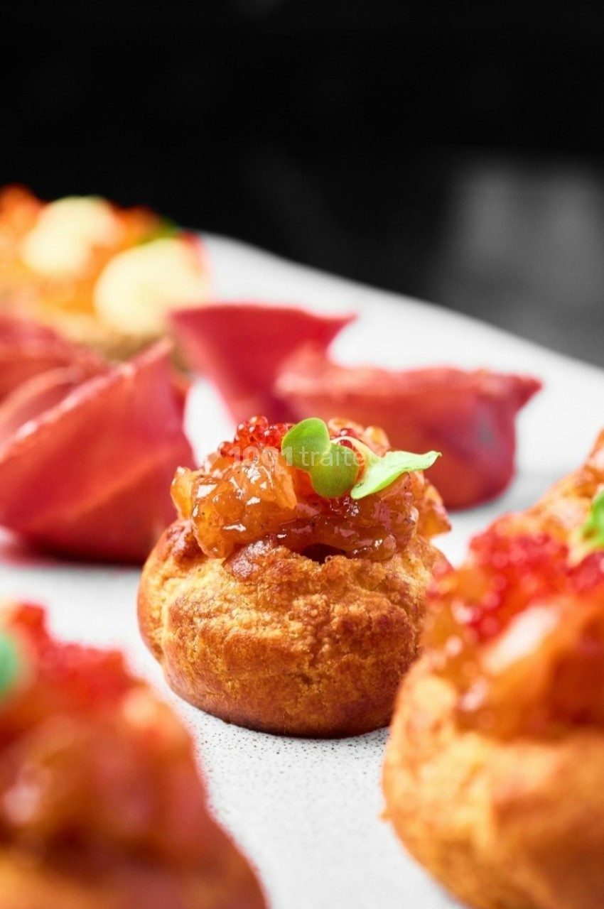 Choux garnis de confit d'oignons, œufs de poisson et micro-pousses, servis sur une assiette blanche.