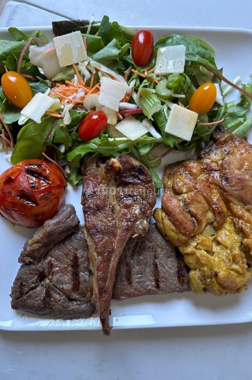 Assiette composée de viande grillée, ris de veau, salade verte garnie de légumes et fromage, et tomate grillée.