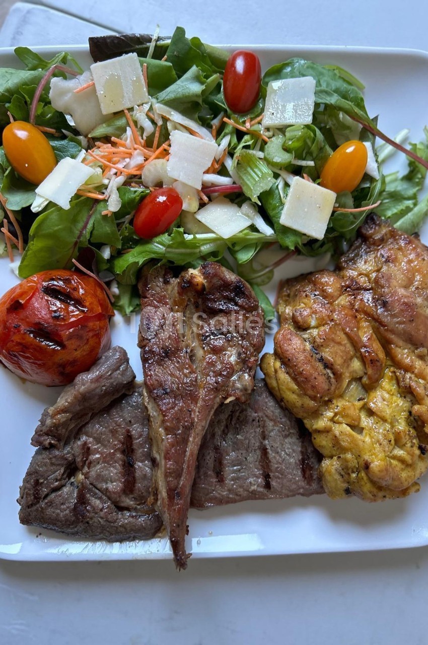 Assiette composée de viande grillée, ris de veau, salade verte garnie de légumes et fromage, et tomate grillée.