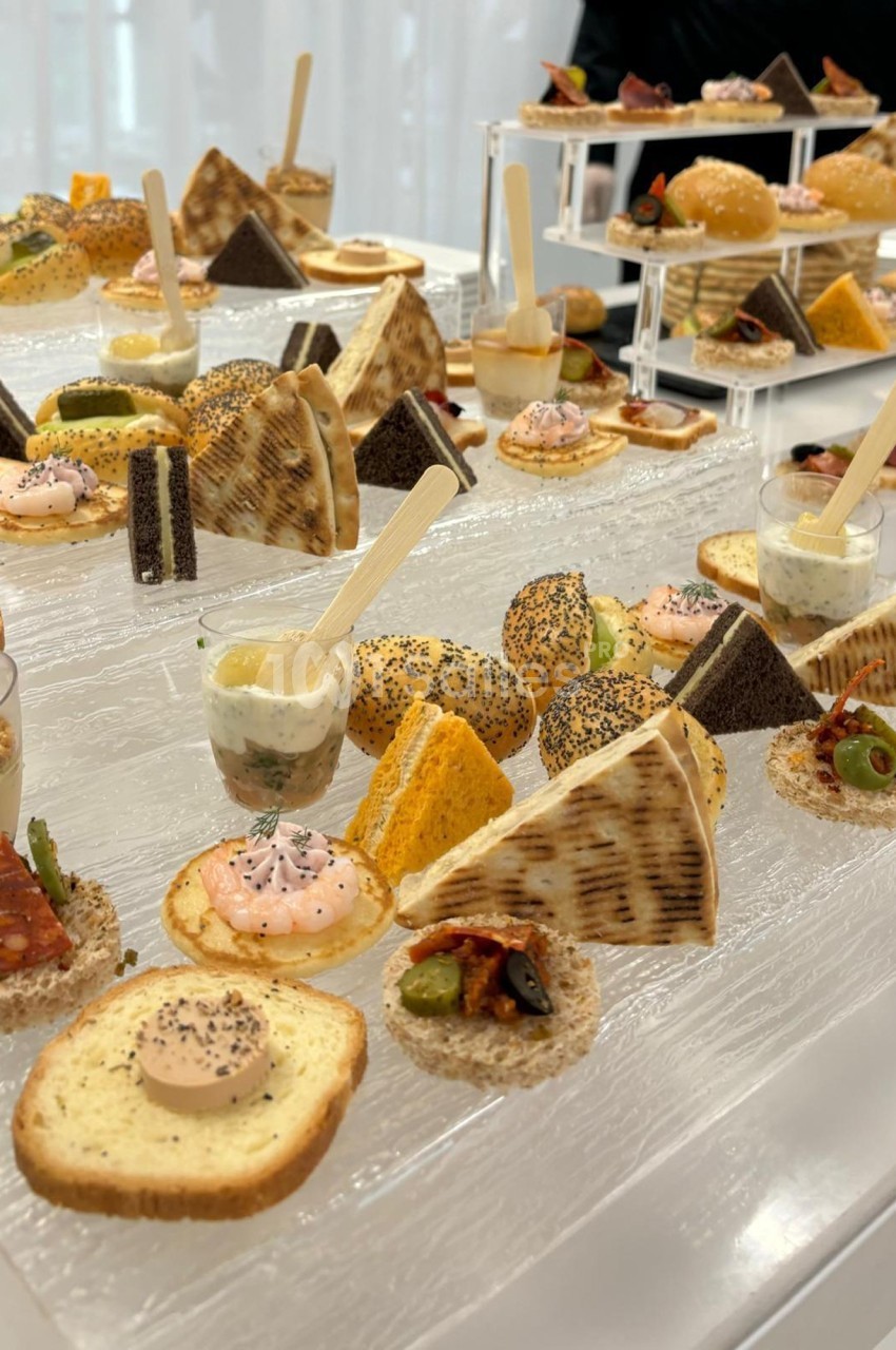 Plateau de bouchées apéritives variées, incluant toasts, verrines et mini-sandwiches, disposées sur une table.