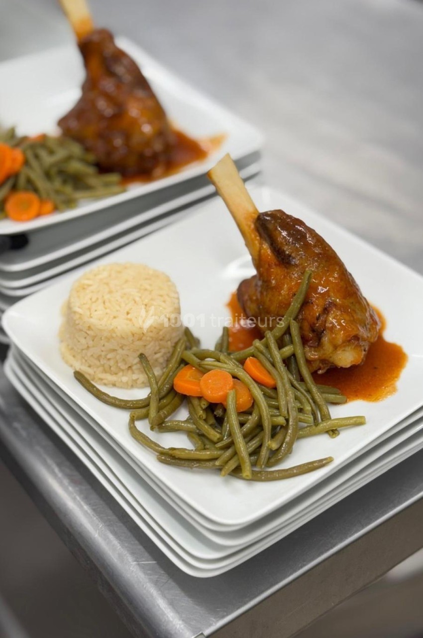 Assiette contenant un jarret d'agneau en sauce, du riz, des haricots verts et des rondelles de carottes.